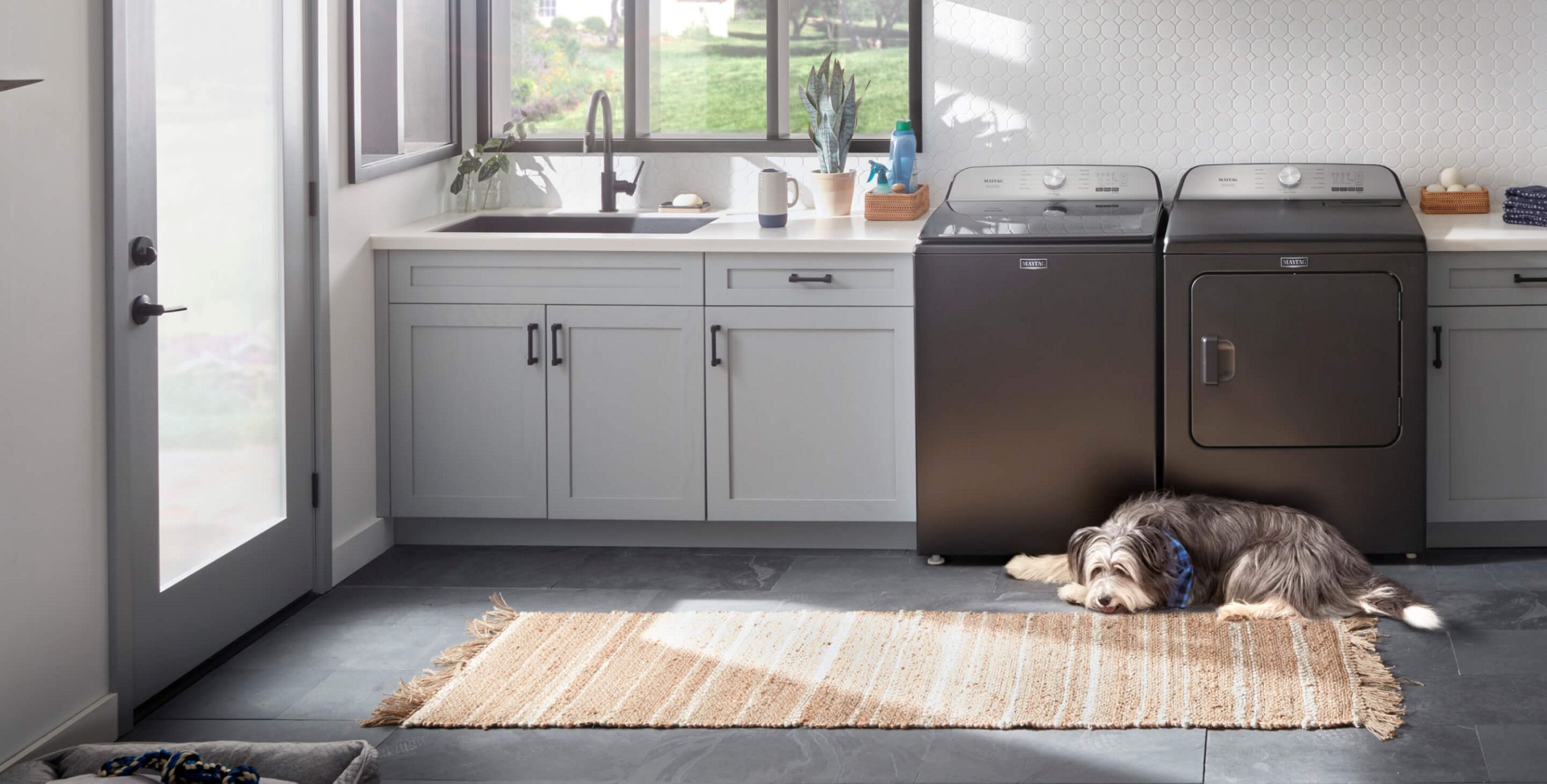 A laundry room with a dog laying in front of the Maytag® Pet Pro washer and dryer pair.