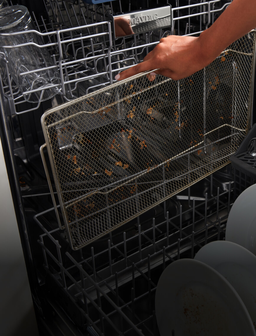 A used air fry basket getting placed into the dishwasher.