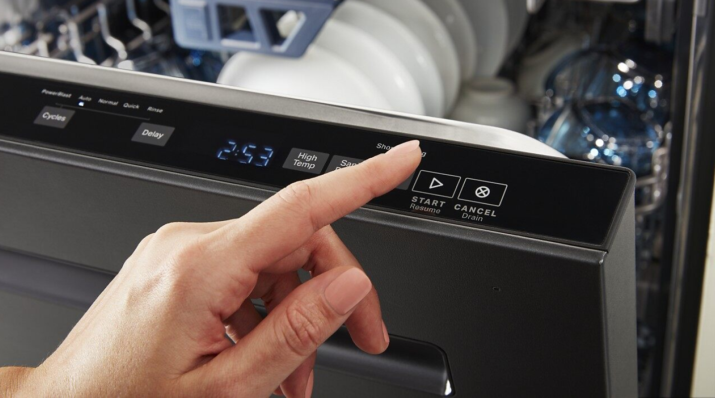 Hand pressing start button on dishwasher panel