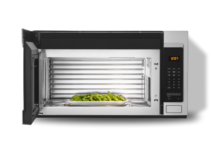 An open microwave with a plate of green beans inside.