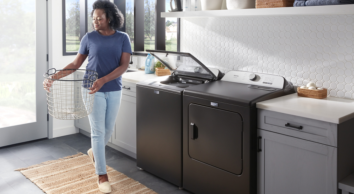 A person doing laundry with a Maytag® washer and dryer set.