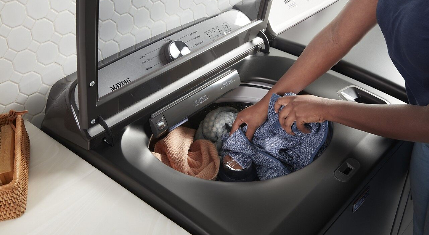 Hands putting laundry into top load washer