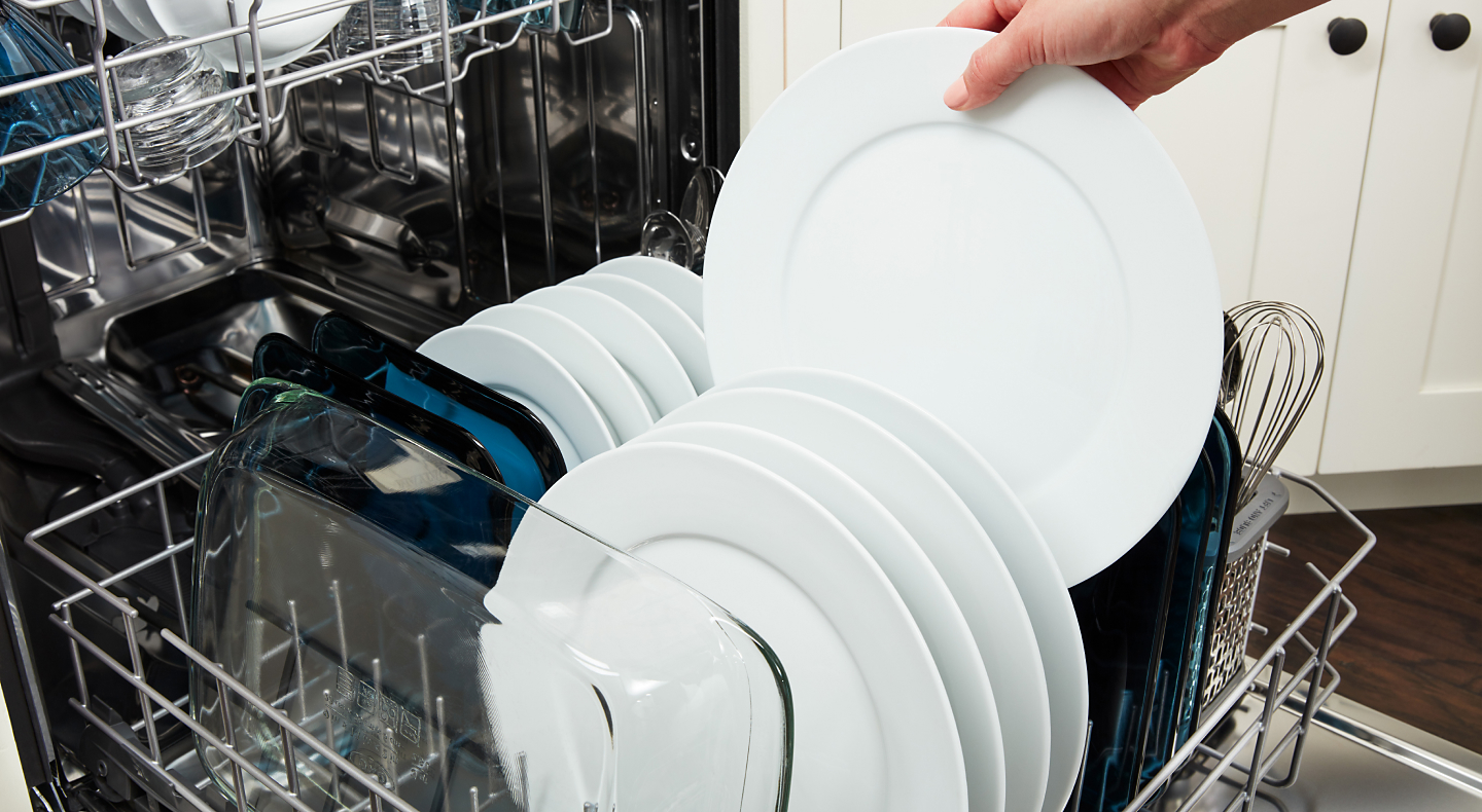 A person pulling a clean dish out of a dishwasher rack