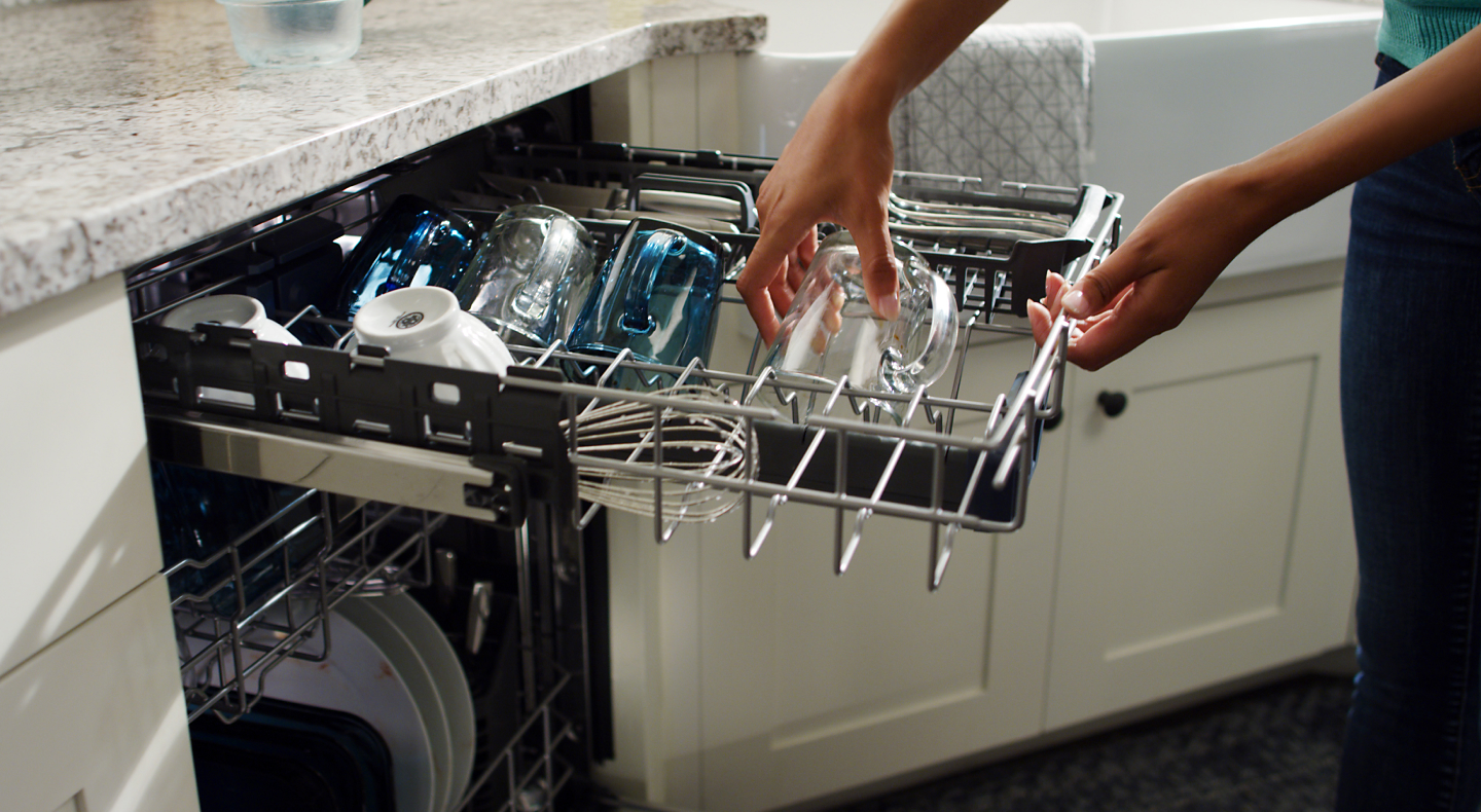 A person pulling a clean glass out of a dishwasher rack
