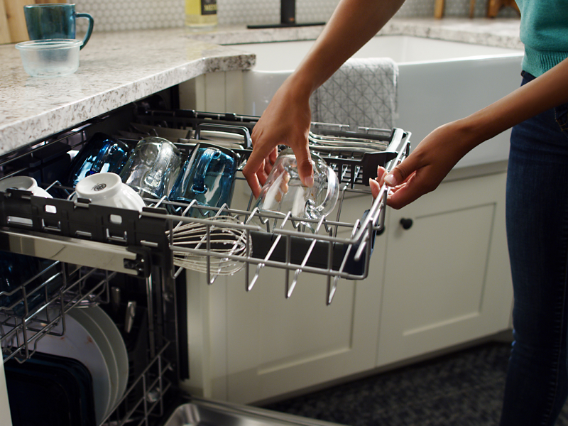 A person pulling a clean glass out of a dishwasher rack