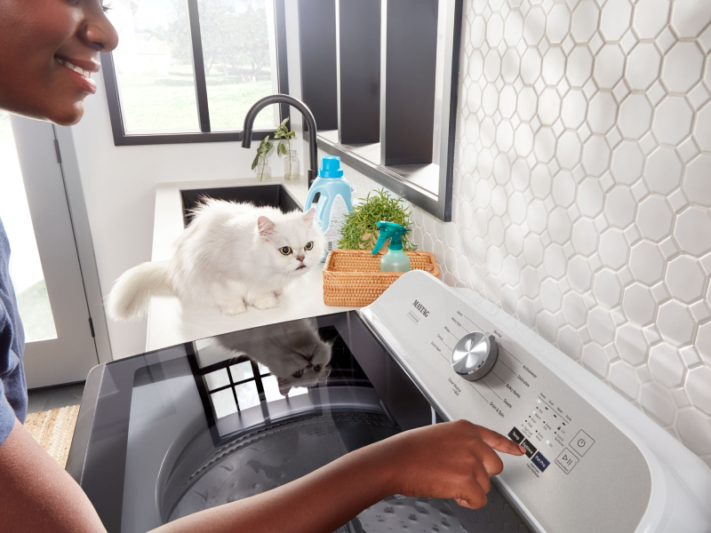 A woman making a selection on a washer next to a cat