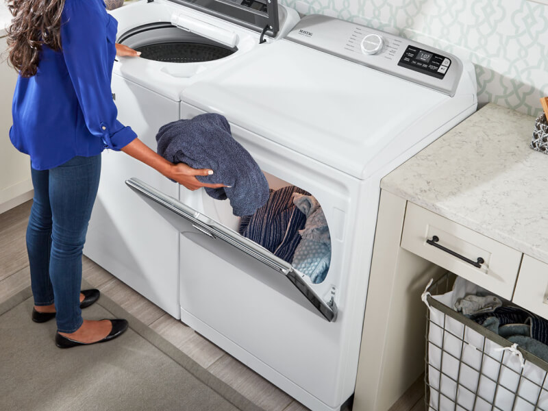 A woman placing a towel into a large capacity dryer 