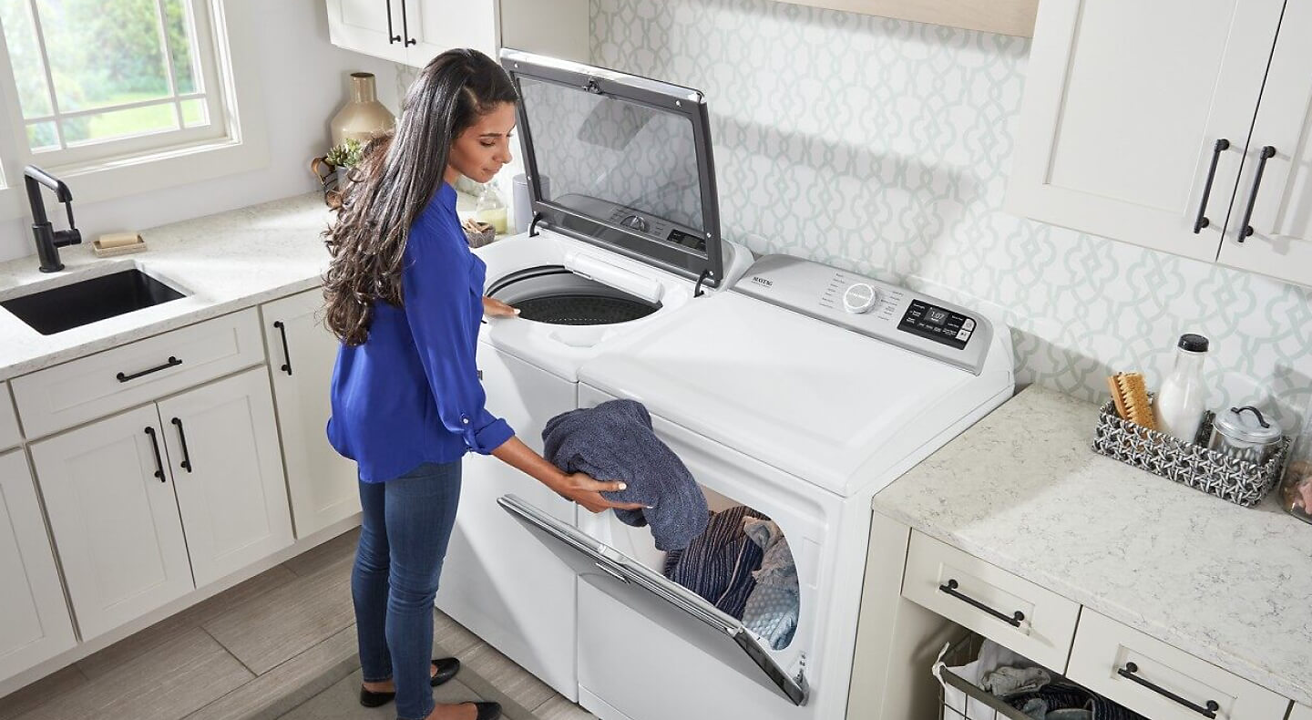 A woman loading washed laundry into a dryer
