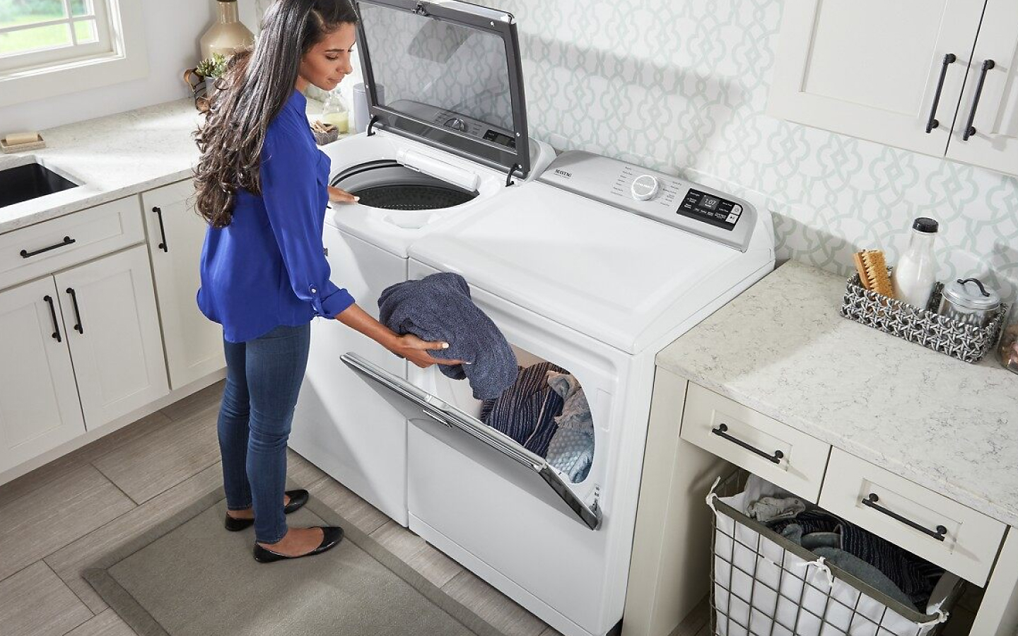 Woman transferring clothes from white top-load MaytagⓇ washer to dryer