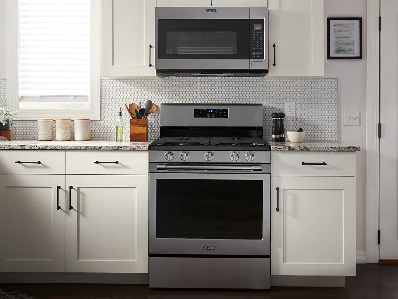 Maytag brand stainless steel range between white cabinetry beneath over-the-range microwave