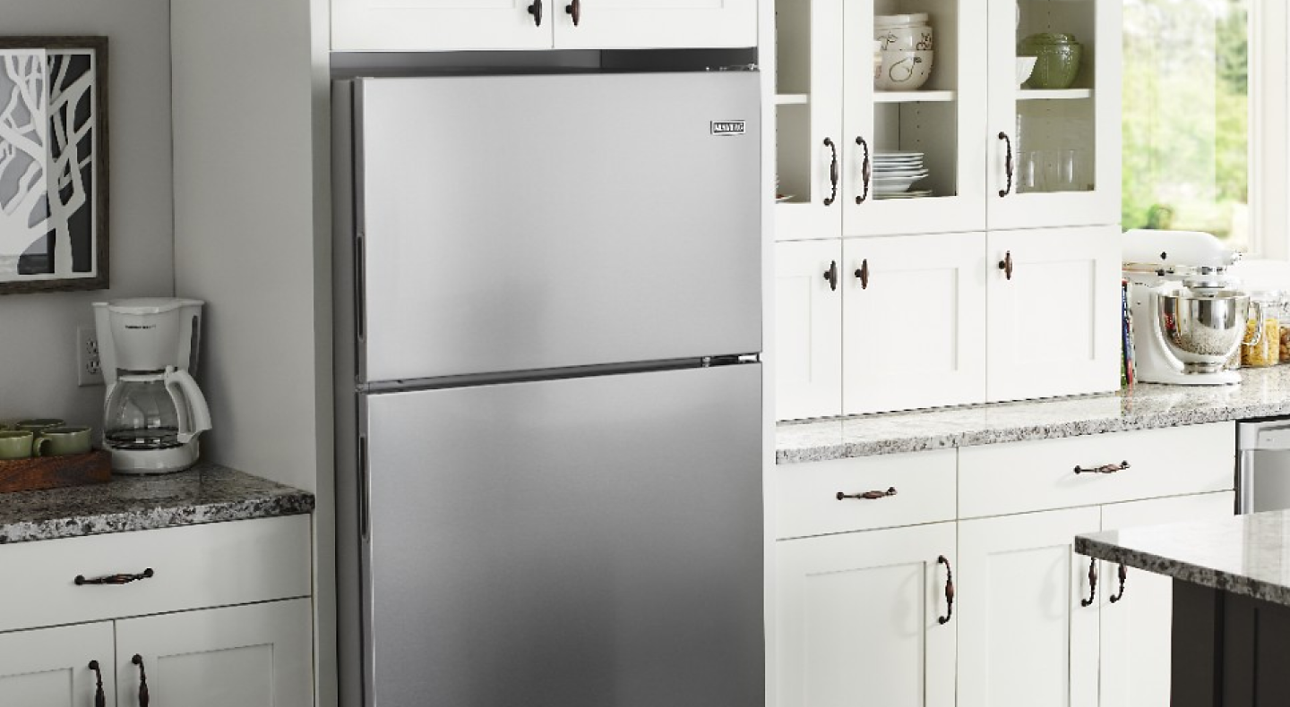 Stainless steel Maytag brand top-freezer refrigerator in kitchen with white cabinets