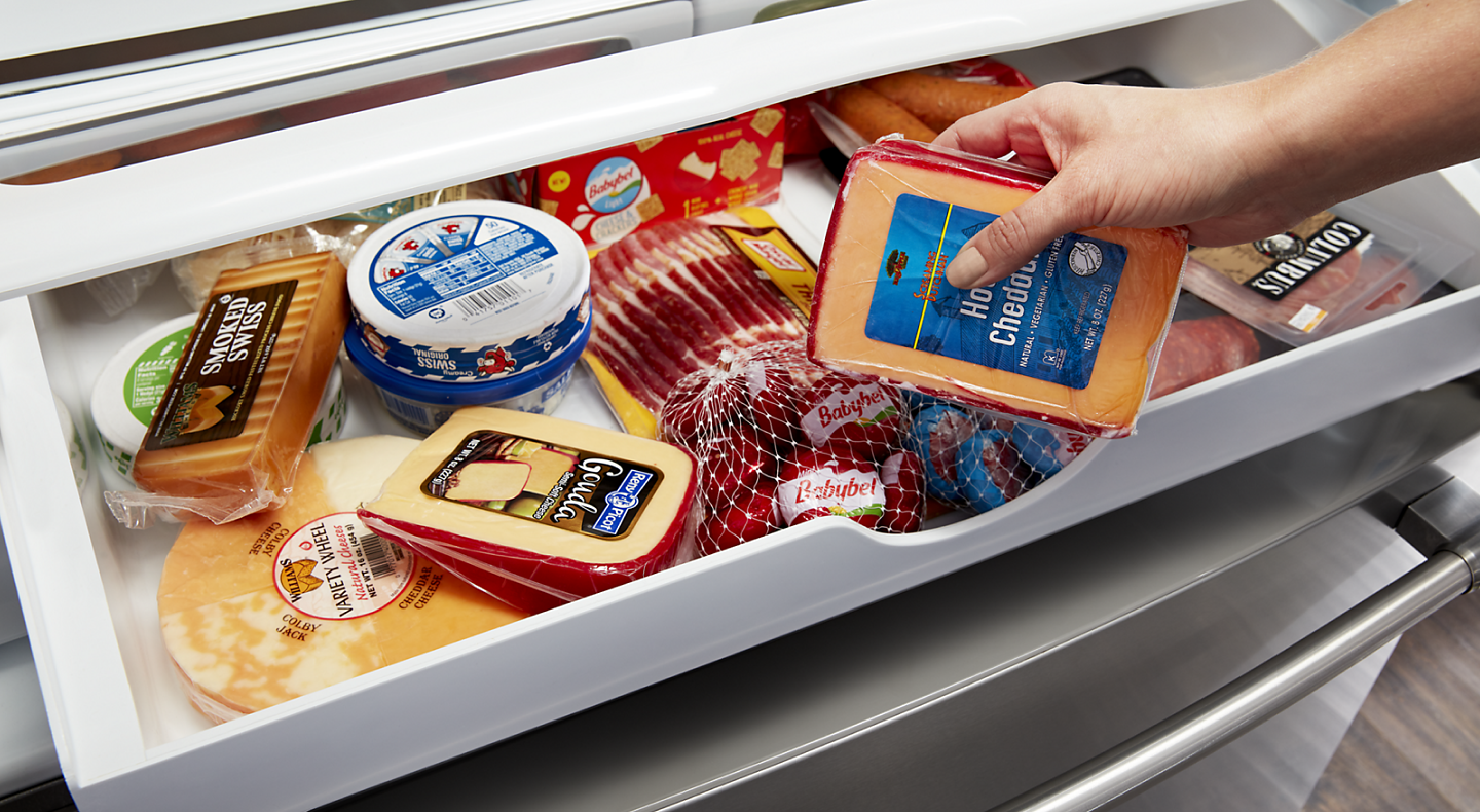 Close-up of person placing cheese in wide deli drawer