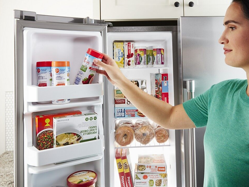 Close-up of person placing an item in the freezer door bin on a side-by-side refrigerator