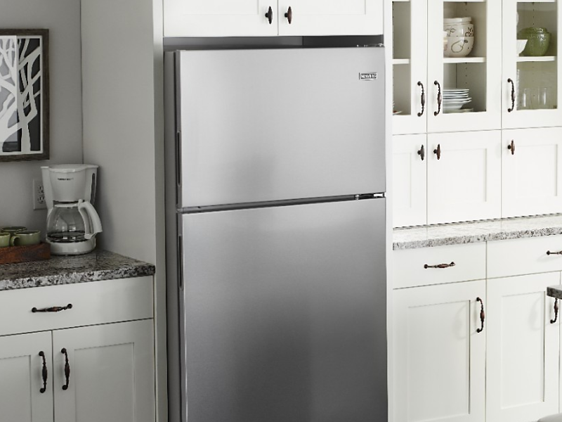 Stainless steel Maytag brand top-freezer refrigerator in kitchen with white cabinets
