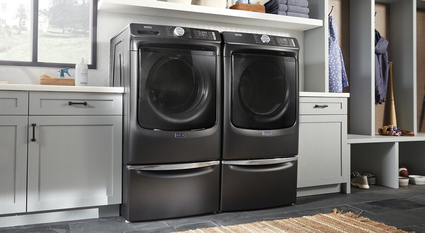 Black Maytag®  front load washer and dryer pair on pedestals in laundry room.
