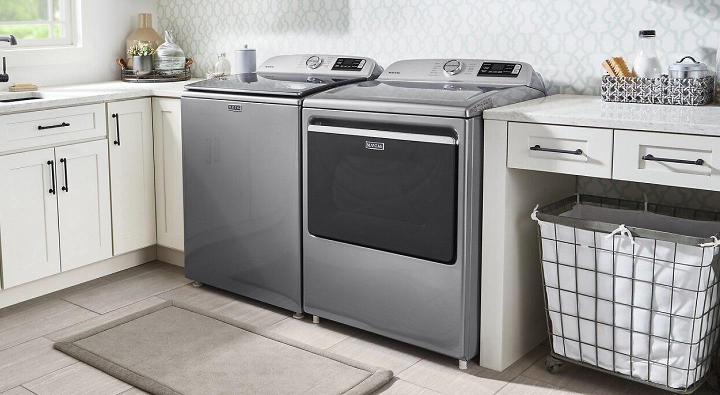 Gray Maytag®  top load washer and dryer pair in laundry room with white cabinetry.