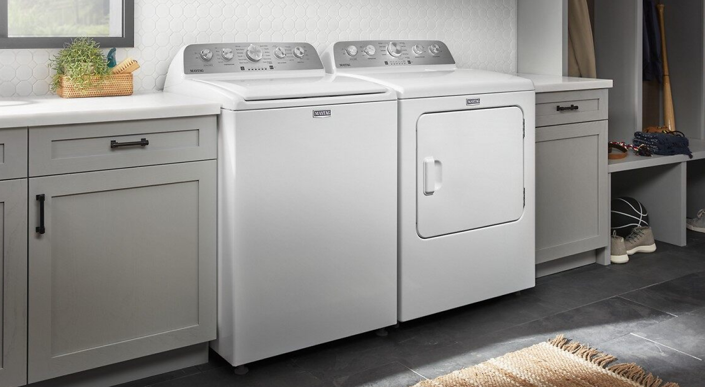 White Maytag® top load washer and dryer pair in gray cabinetry in front of white backsplash.