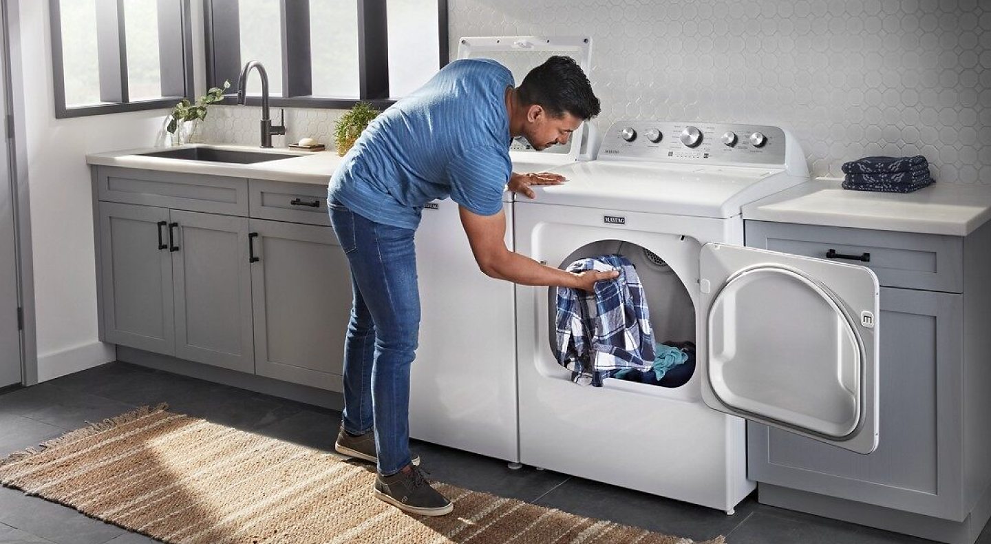 Person loading clothes into an open white Maytag® dryer.