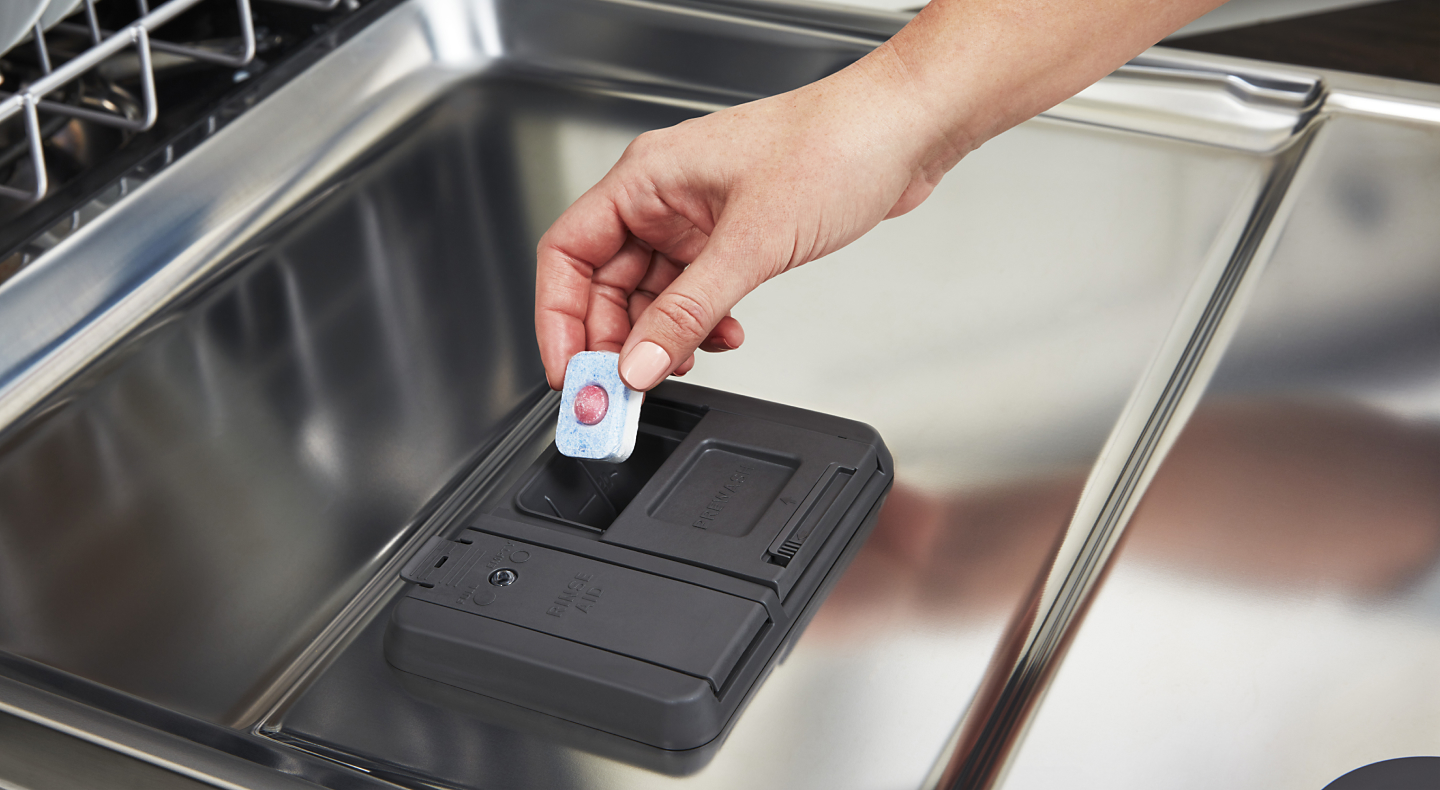 Person placing tablet in dishwasher dispenser