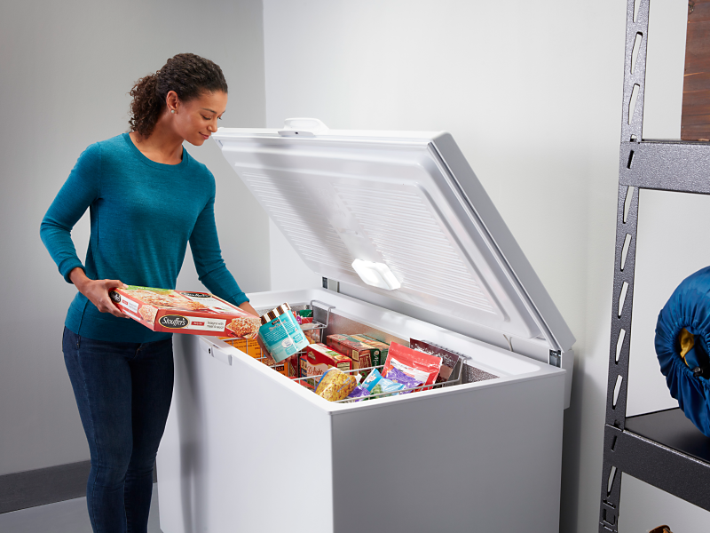 A person removing frozen pasta and ice cream from a garage freezer.