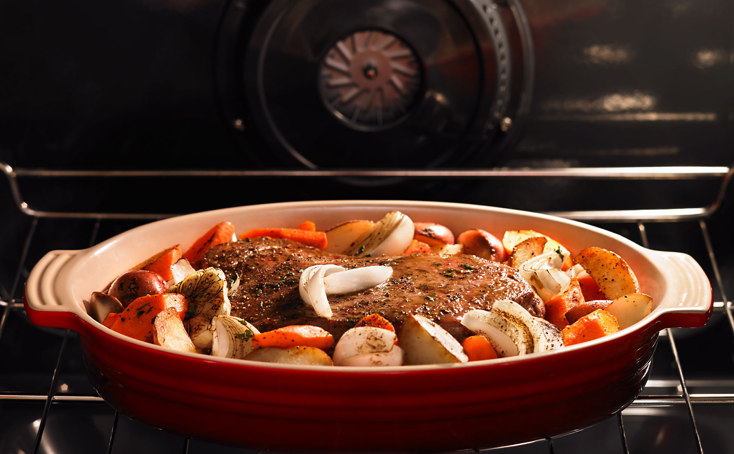 Meat with roasted vegetables cooking in a red baking dish