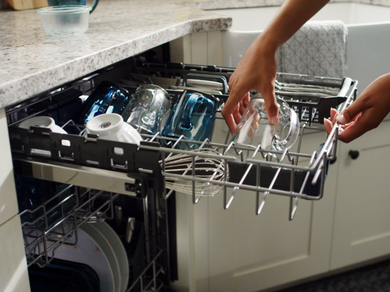 Person loading glasses on a dishwasher third rack.