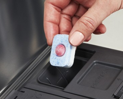 Person placing tablet in dishwasher dispenser