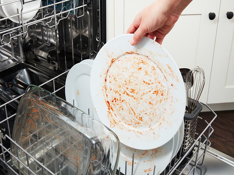 Person placing dirty dishes on dishwasher rack