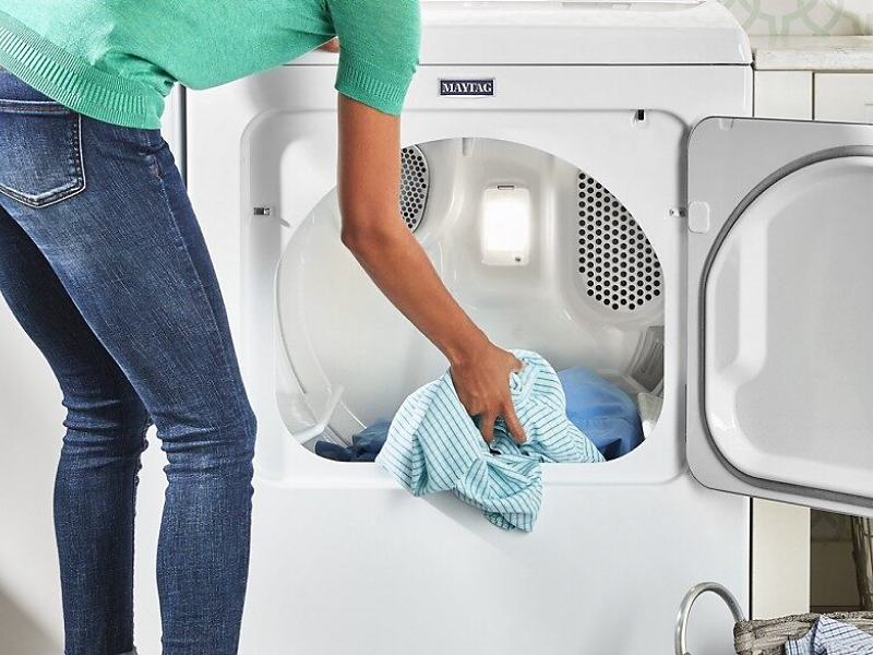 User adding clothes to white front load dryer
