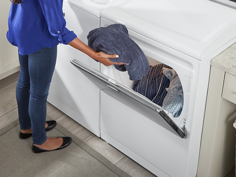 User transferring clothes from white top load washer to white front load dryer
