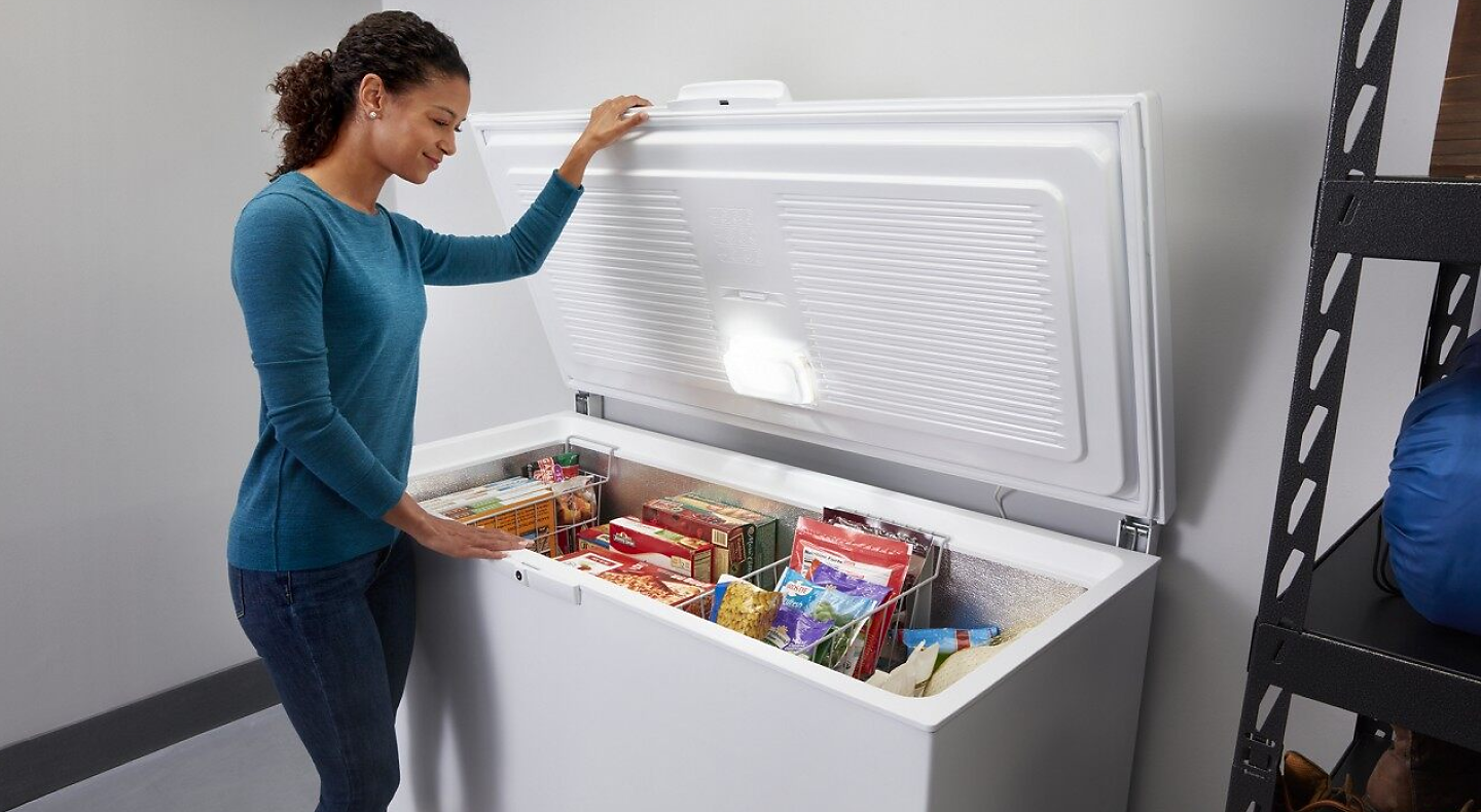 Person opening the door of a white chest freezer full of food
