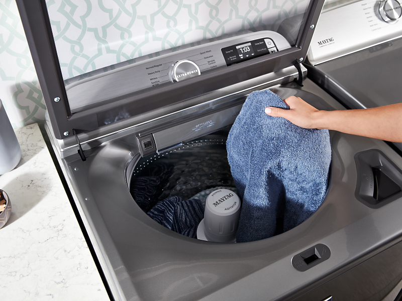 A person placing a towel into a Maytag® Top Load Washer