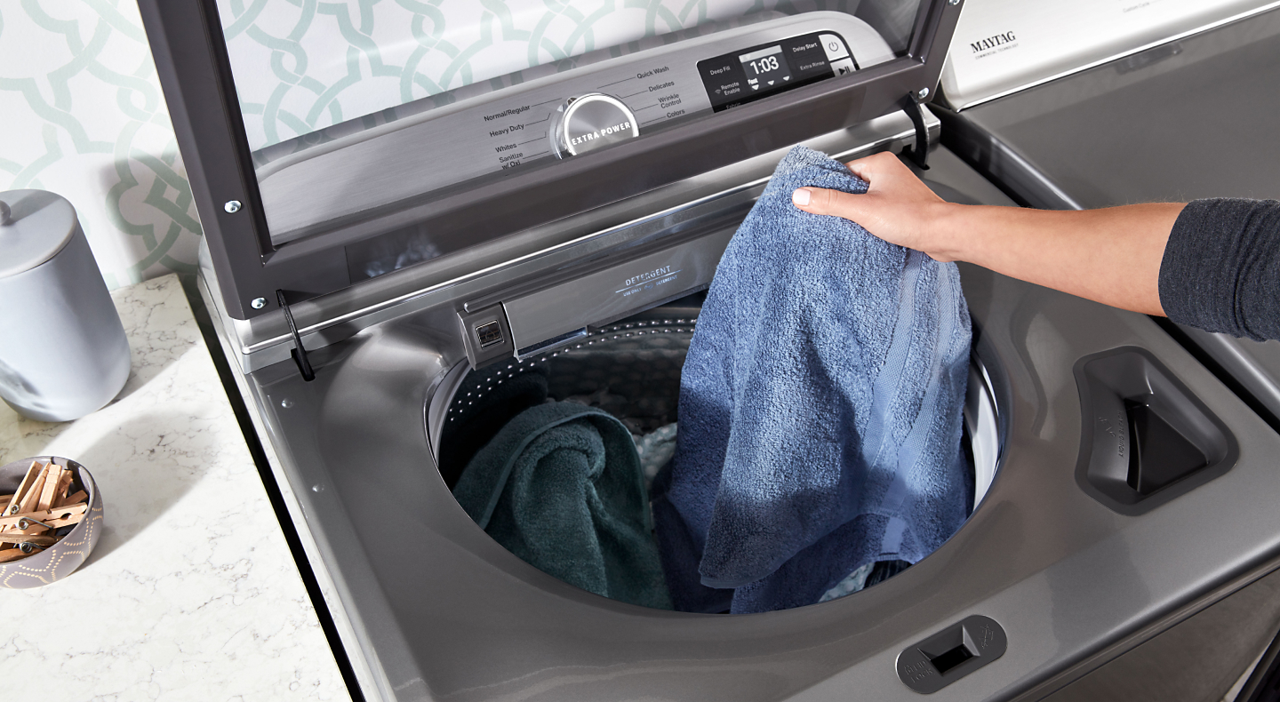 Laundry being added to a metallic slate Maytag® top loading washer