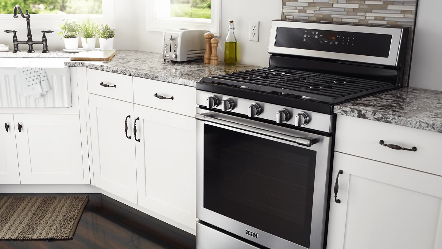 Maytag® gas range installed between white kitchen cabinets