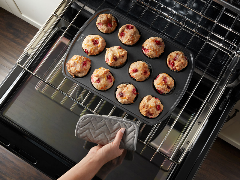 A person removing a tray of muffins from the oven.