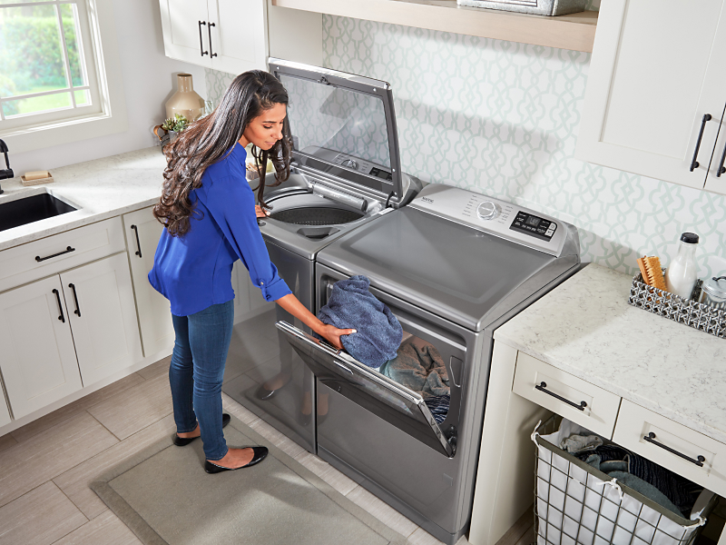 A person doing laundry with a Maytag® side-by-side laundry set.