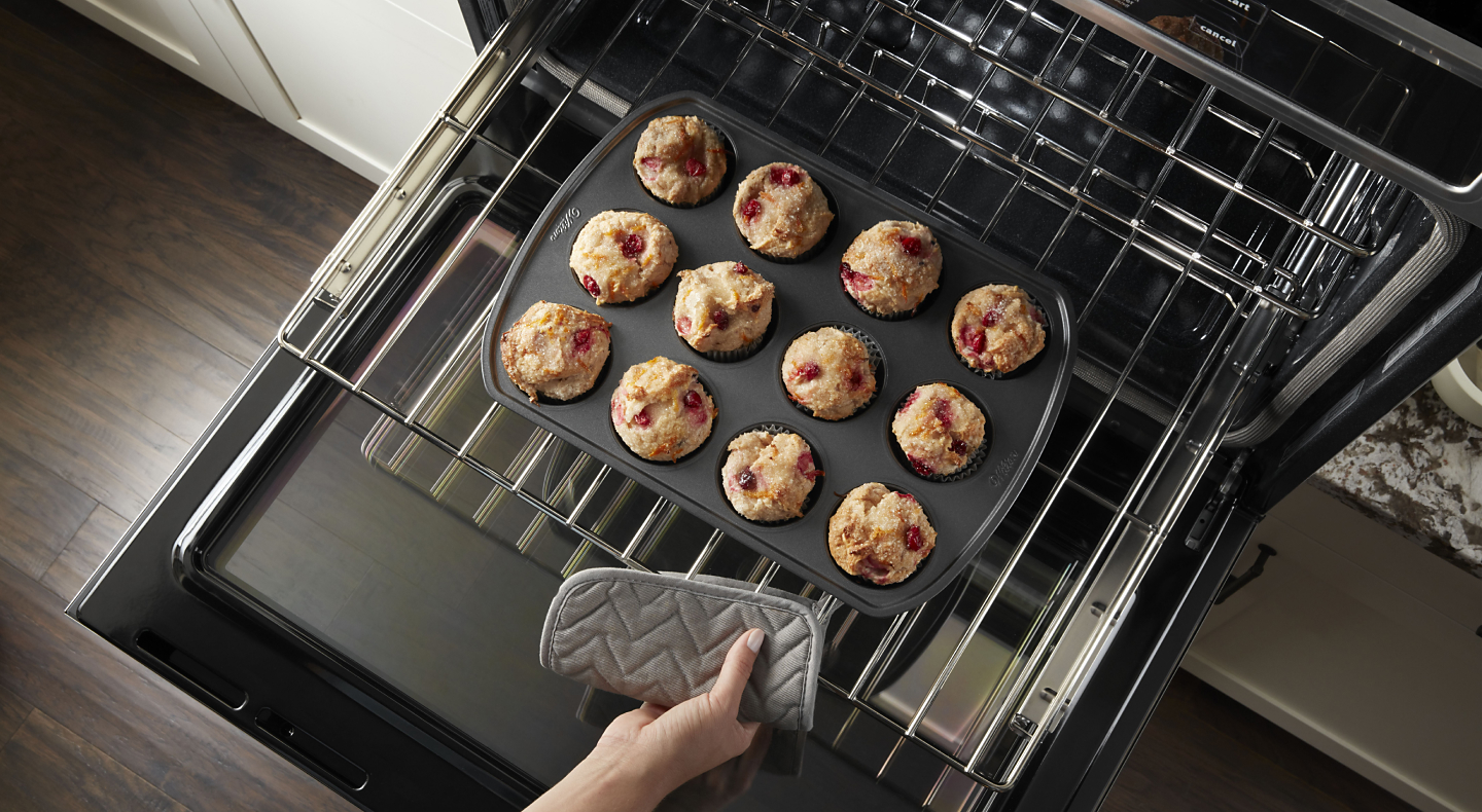 Close-up of a person pulling out freshly baked berry muffins from the middle tray of an oven.