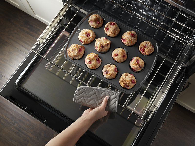 Close-up of a person pulling out freshly baked berry muffins from the middle tray of an oven.