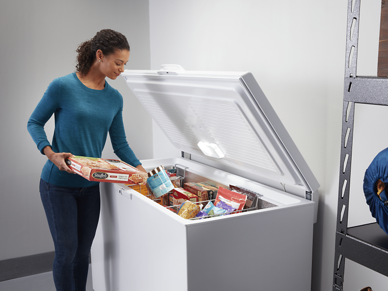 Person loading frozen food into chest freezer baskets