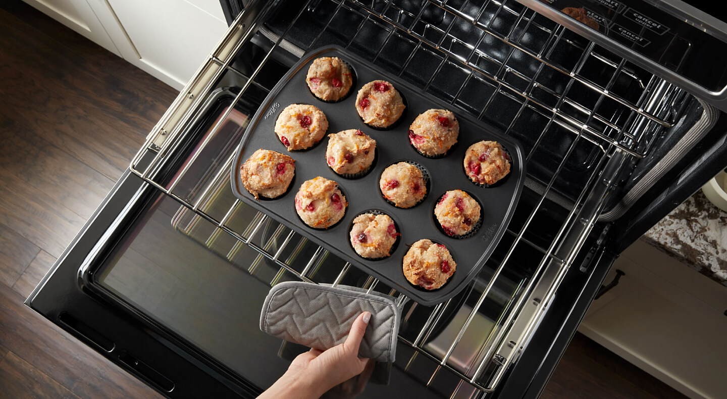 Person pulling muffins out of an oven Person pulling muffins out of an oven