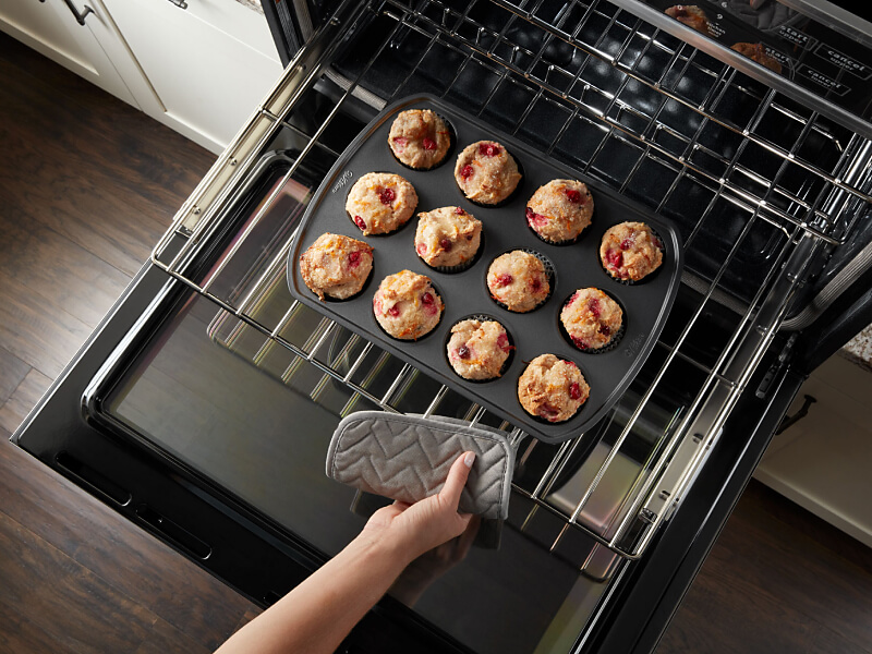 Person pulling muffins out of an oven Person pulling muffins out of an oven