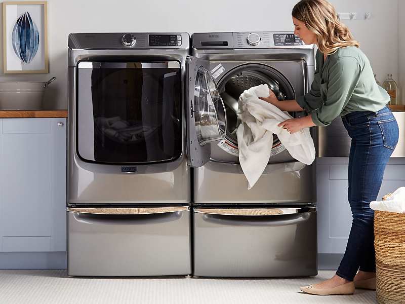 White linens being loaded into a Maytag® washer