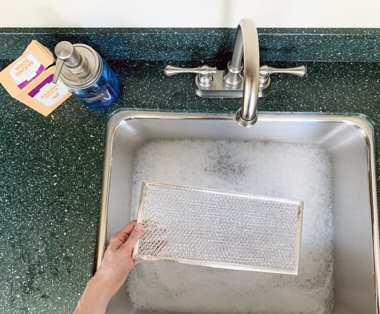 Hand lowering grease filter into sink with soapy water