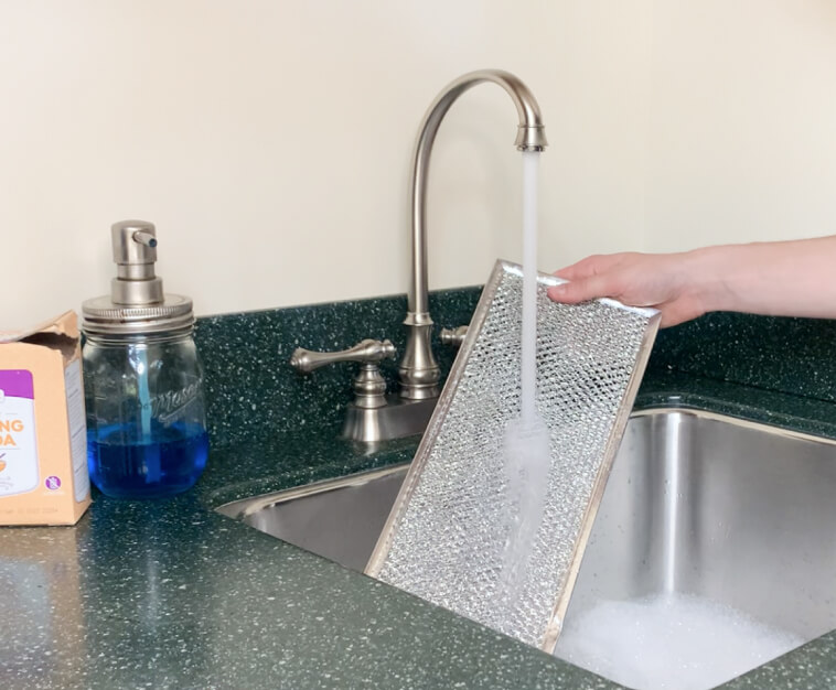 Grease filter being rinsed under a running faucet 
