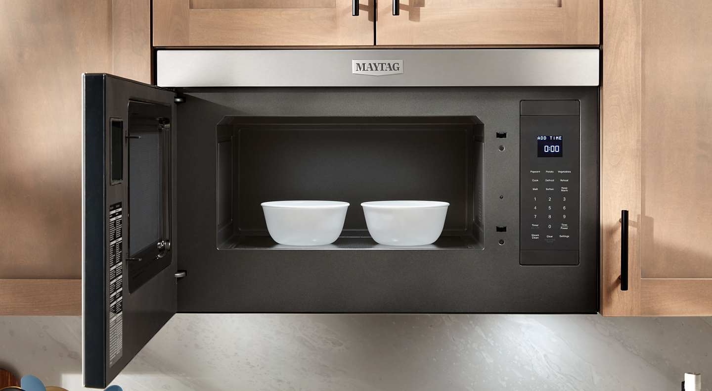 Two side-by-side glass bowls in an open Maytag® over-the-range microwave