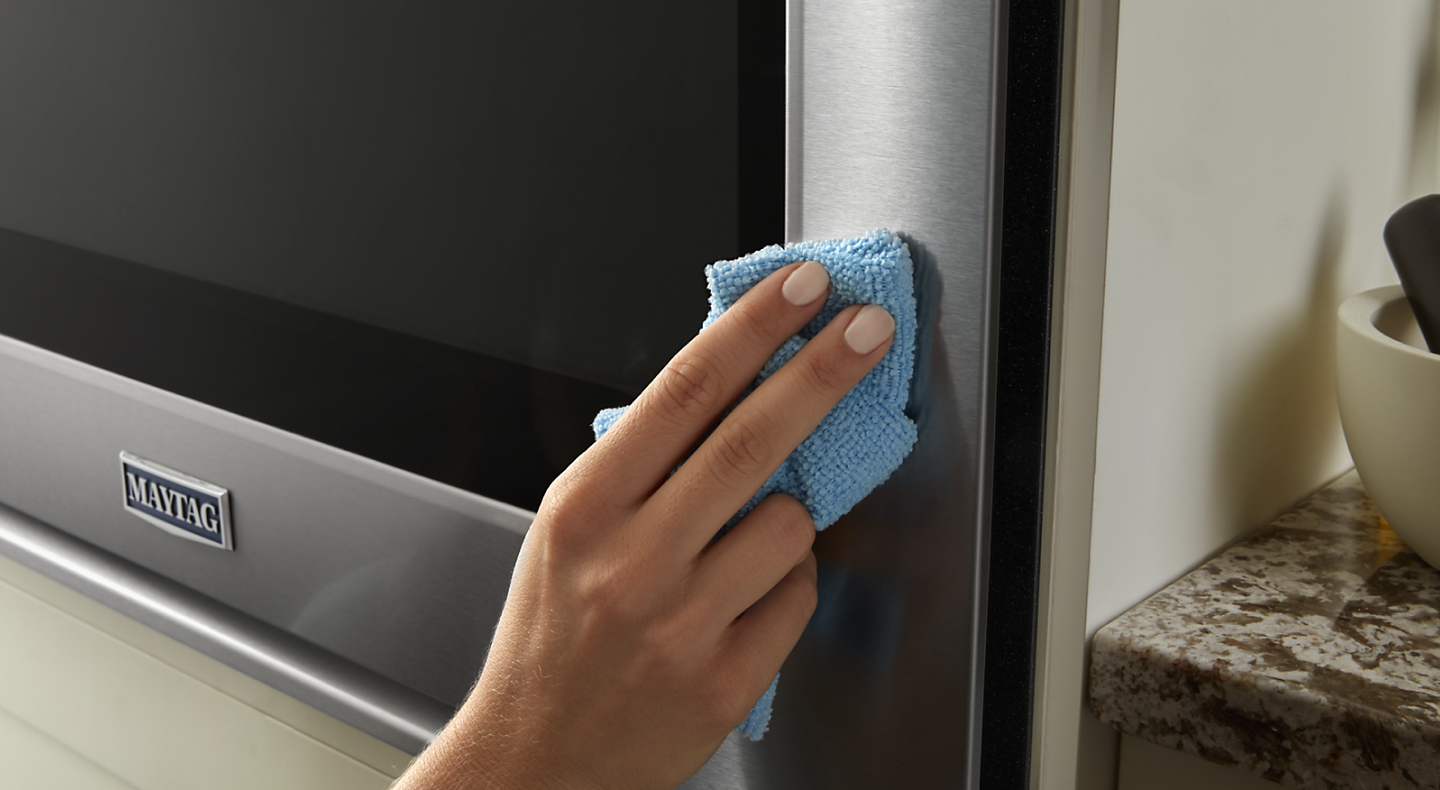 A person wipes down the stainless steel exterior of a Maytag® oven.