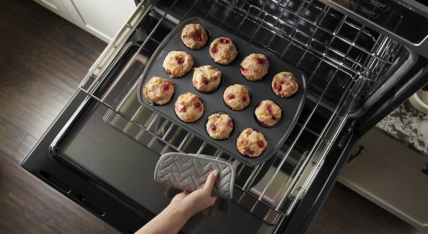 Person pulling rack from oven with muffin pan