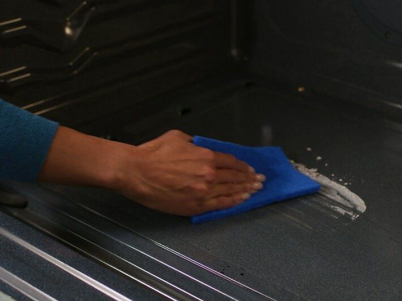 A person wipes down the bottom of an oven.