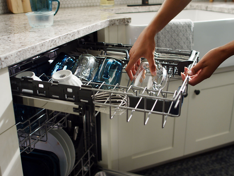 Person placing glasses on third-level rack of dishwasher