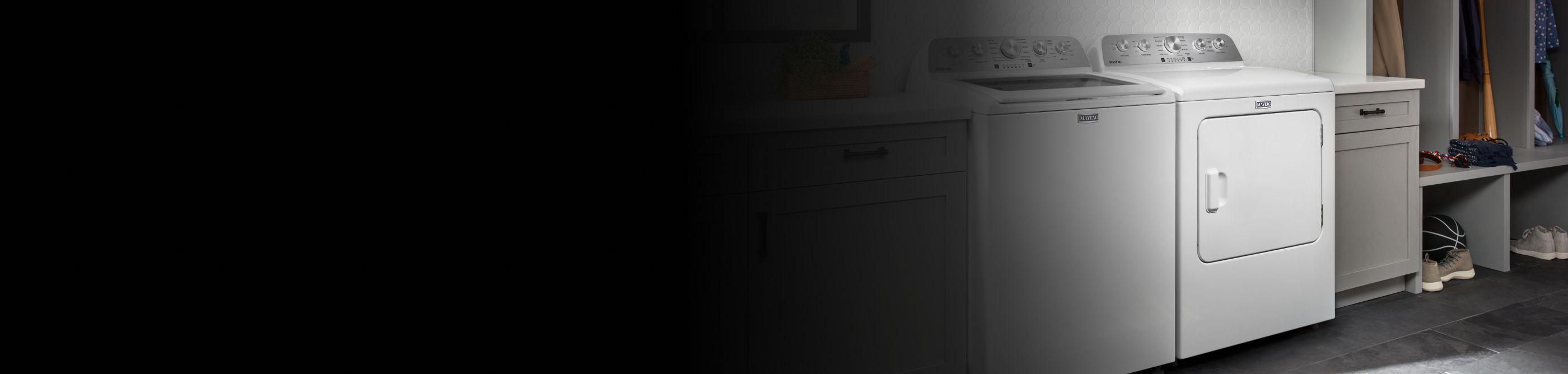 White Maytag® top load washer and front load dryer side by side in a laundry room next to shelves